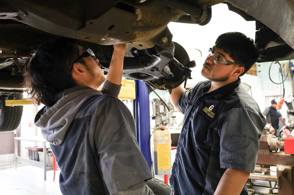 two students standing underneath car in car lift
