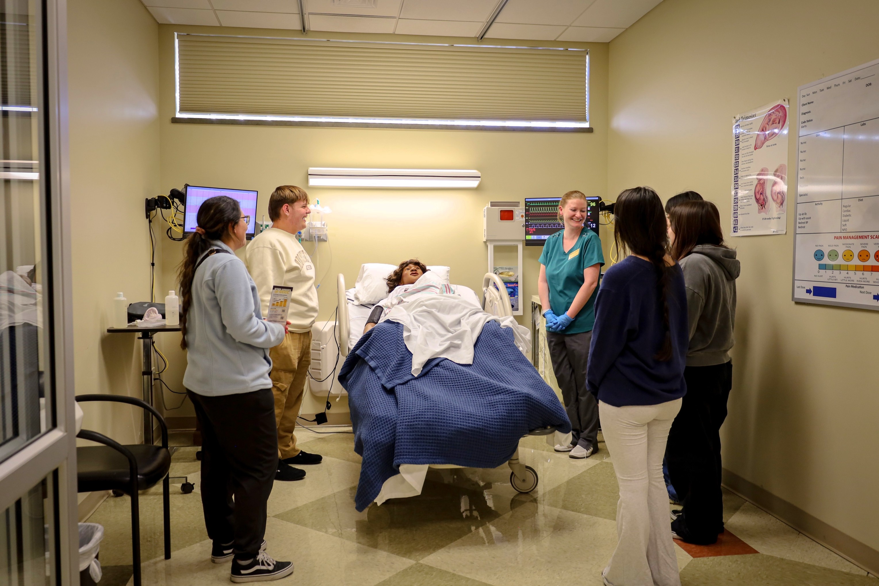A group of healthcare professionals gathered around a hospital bed in a patient room, with one patient lying under a blanket.