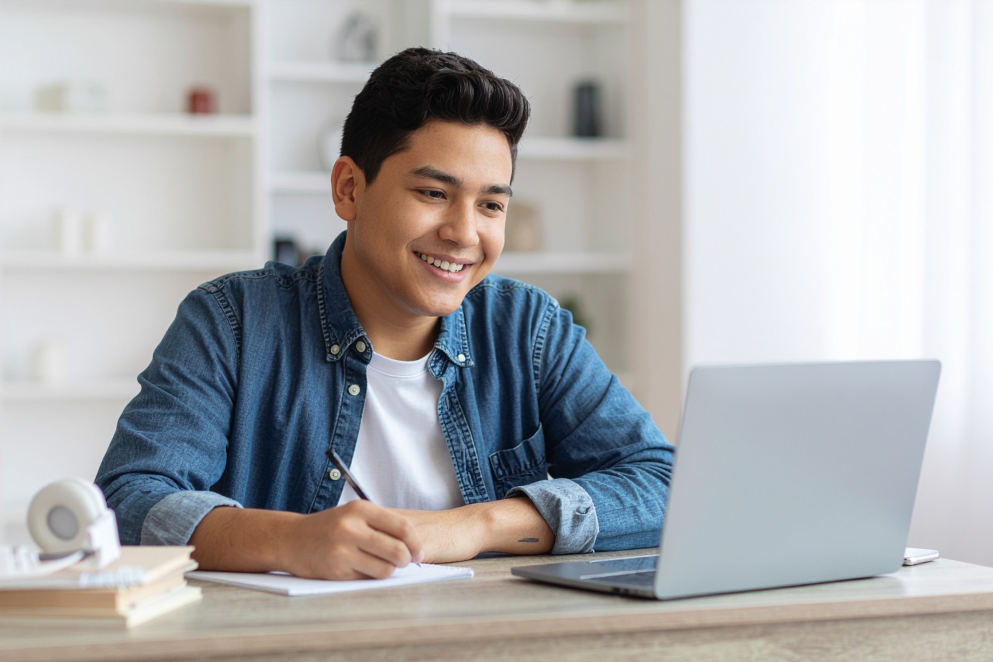 Student participates in an online class, writing notes while using a laptop at home.