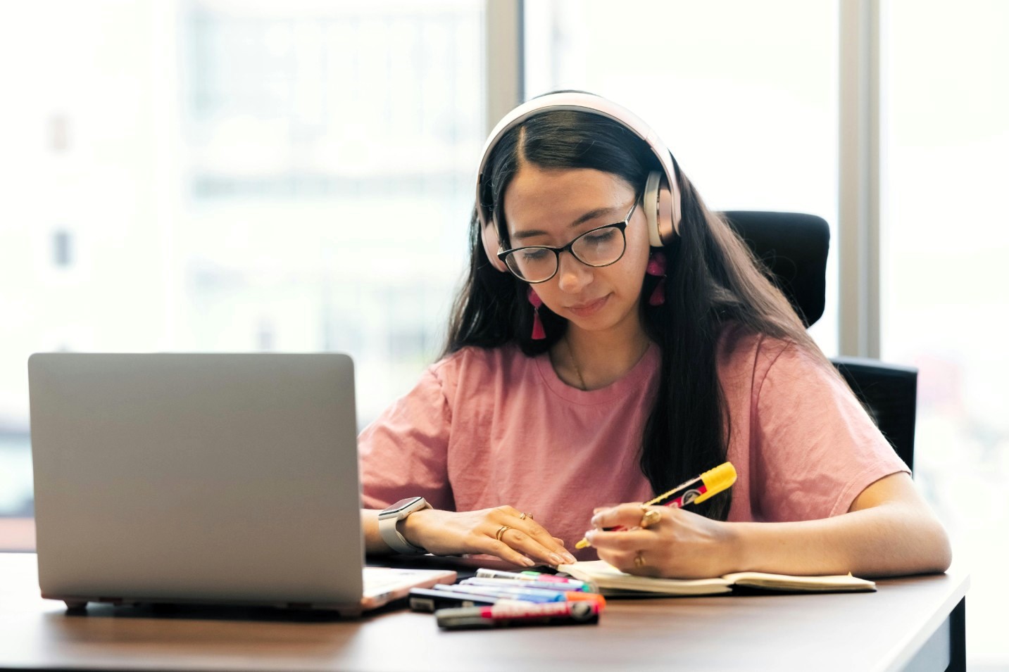 Student wearing headphones takes notes beside a laptop during an online learning session.