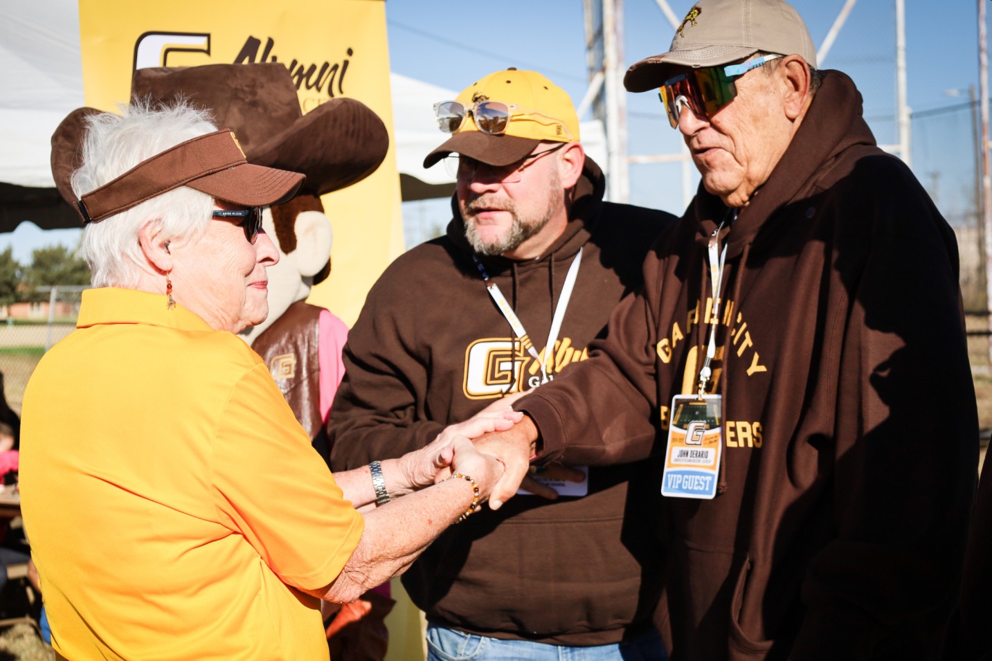Alumni greeting and handshake at Garden City Community College event with mascot in background.