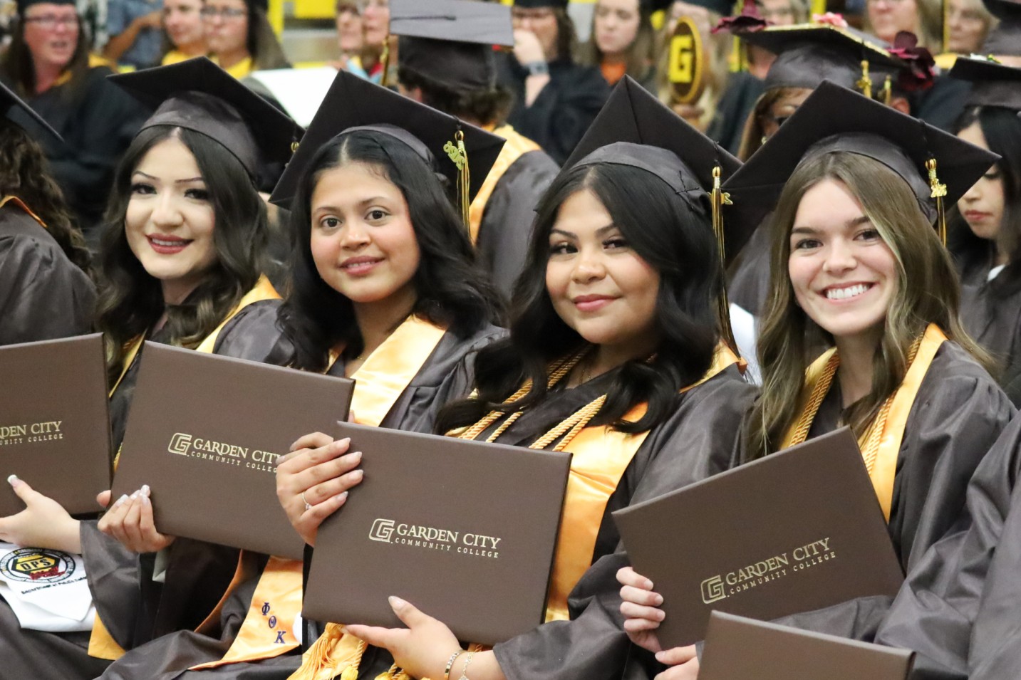Group of graduates in caps and gowns holding Garden City Community College diplomas during a ceremony.