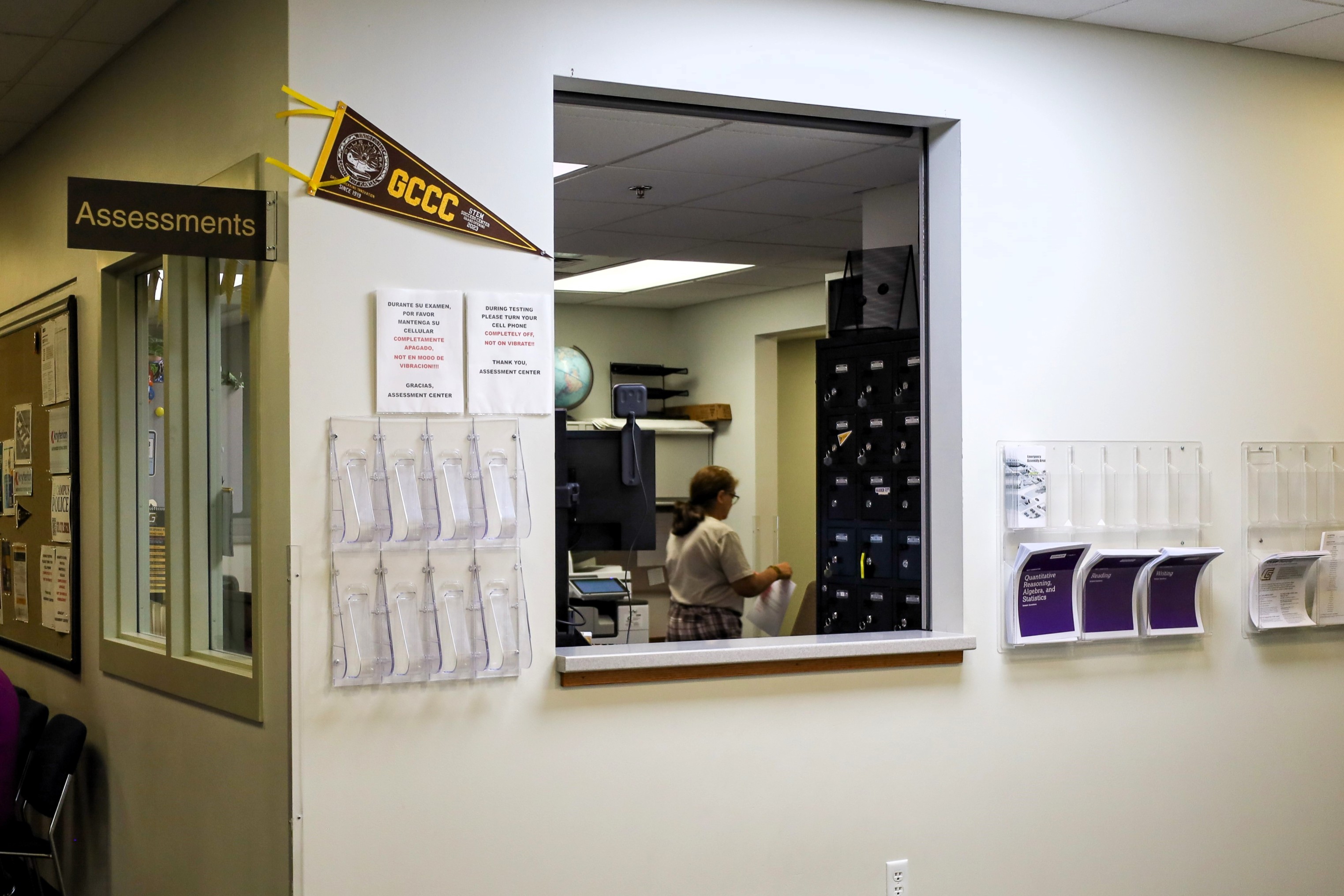Assessment office window with posted signs, pamphlet holders, and a staff member working inside near lockers.