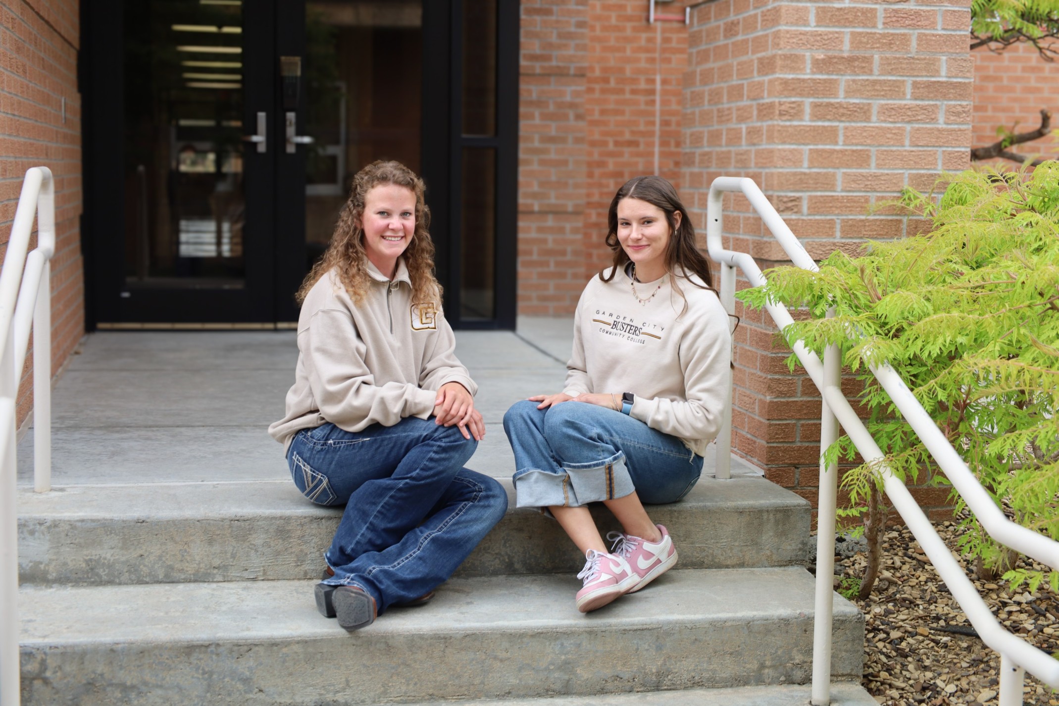 Two people sitting on outdoor steps in front of a brick campus building entrance. Provide your feedback on BizChat