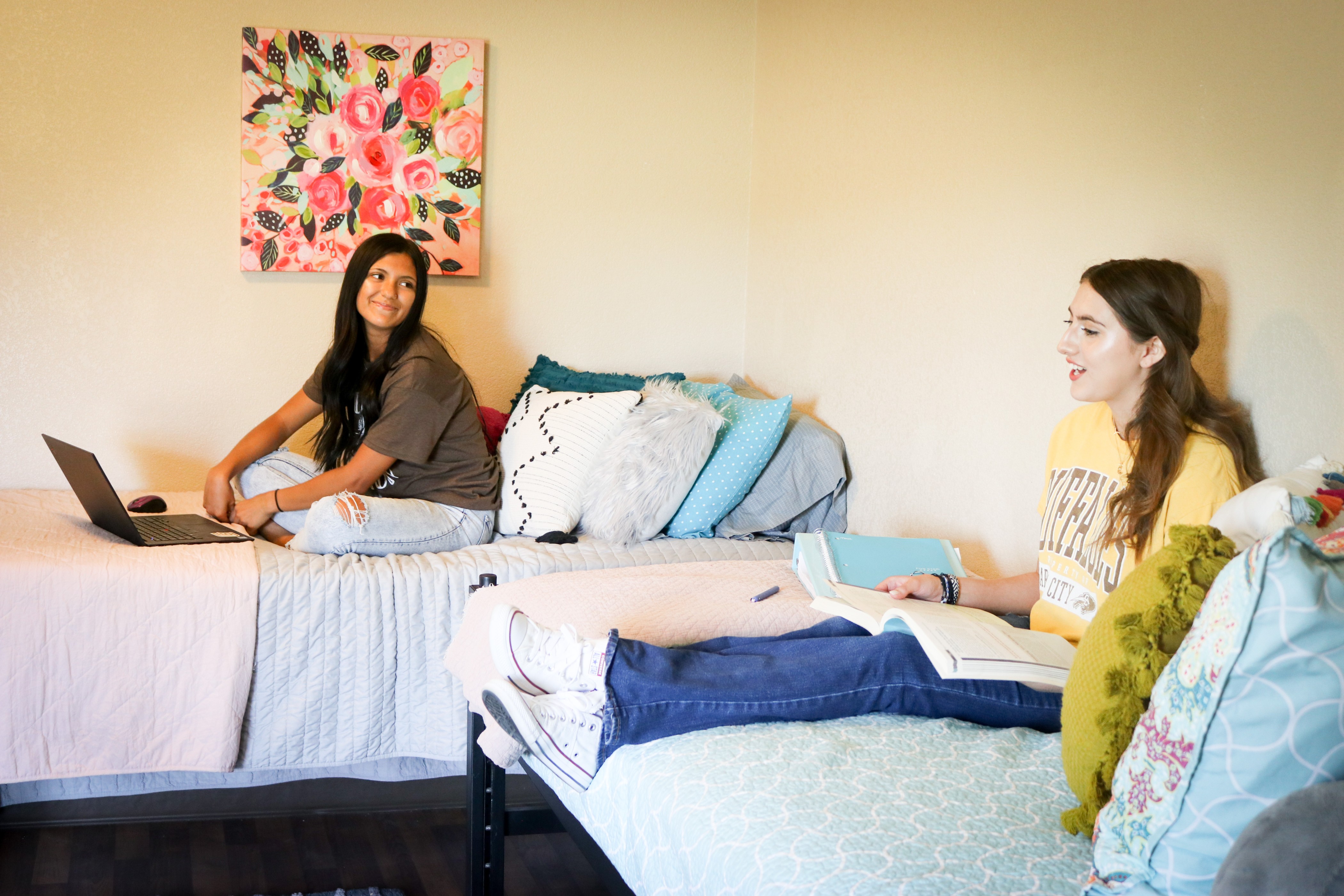 Students studying and relaxing in a residence hall room with beds, books, and a laptop.  Provide your feedback on BizChat