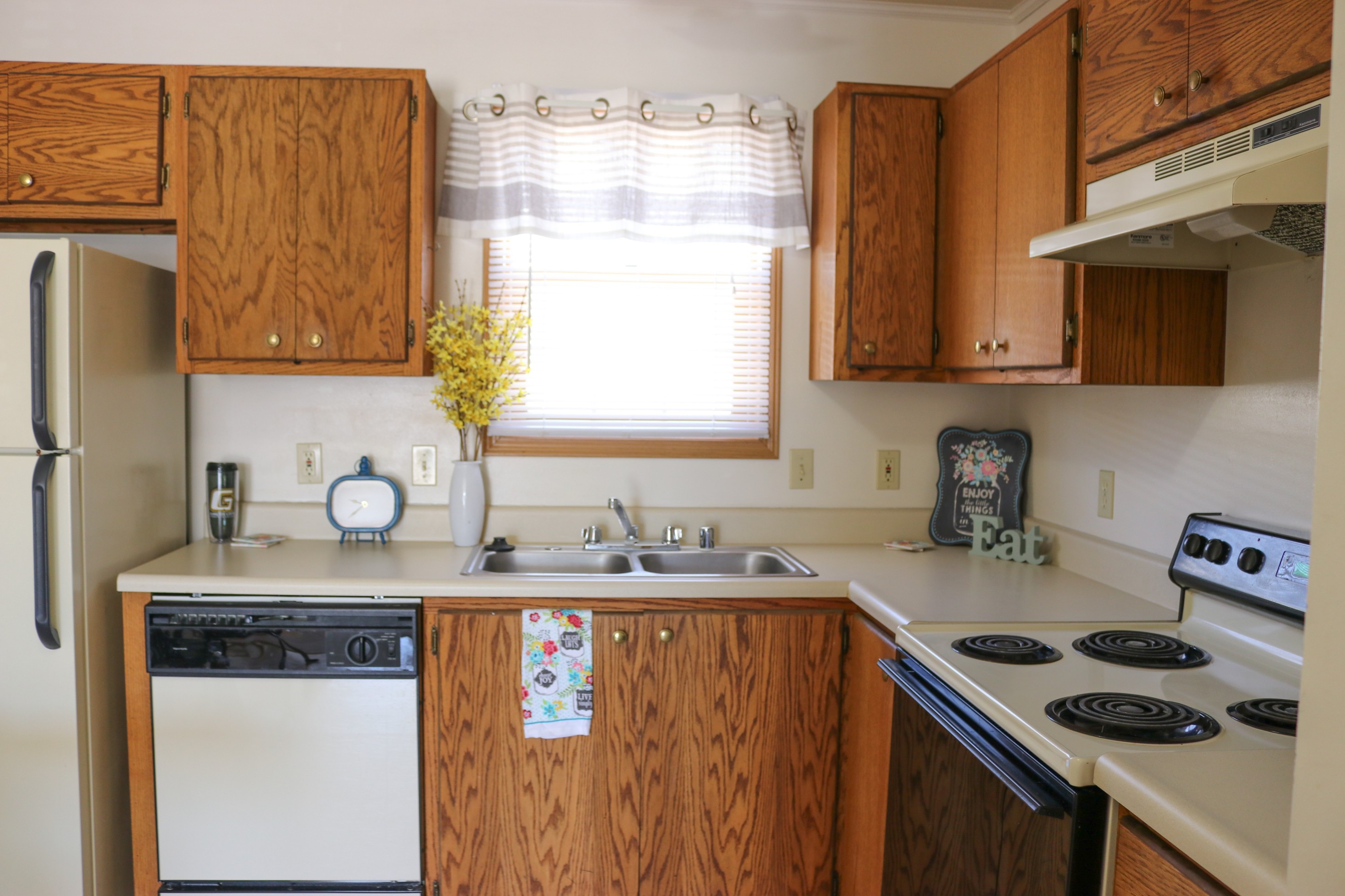 Kitchen with wood cabinets, sink under a window, stove, dishwasher, and small decorative items on the counter.