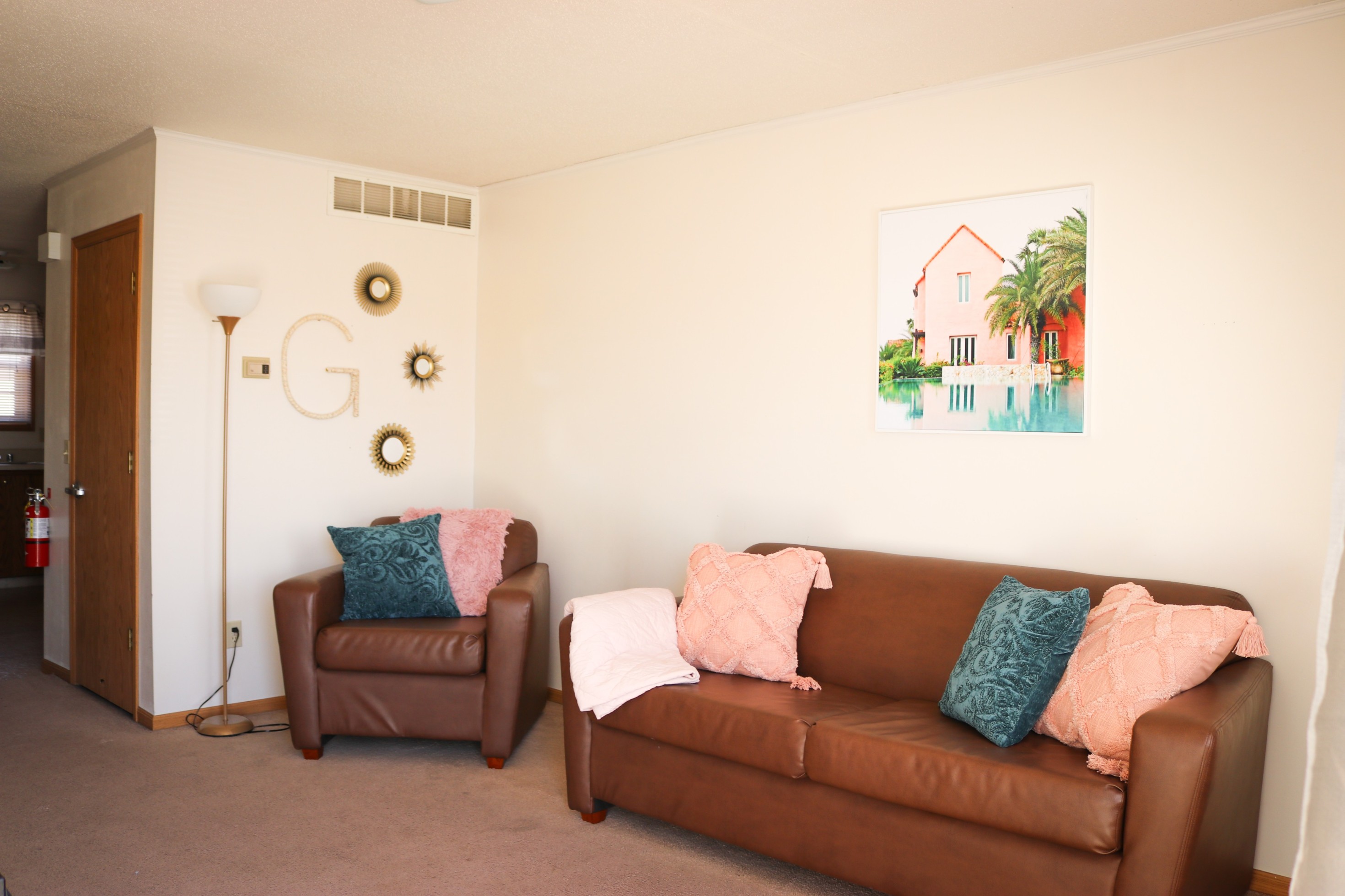 Living room with brown sofa and chair, decorative pillows, wall art, and floor lamp.