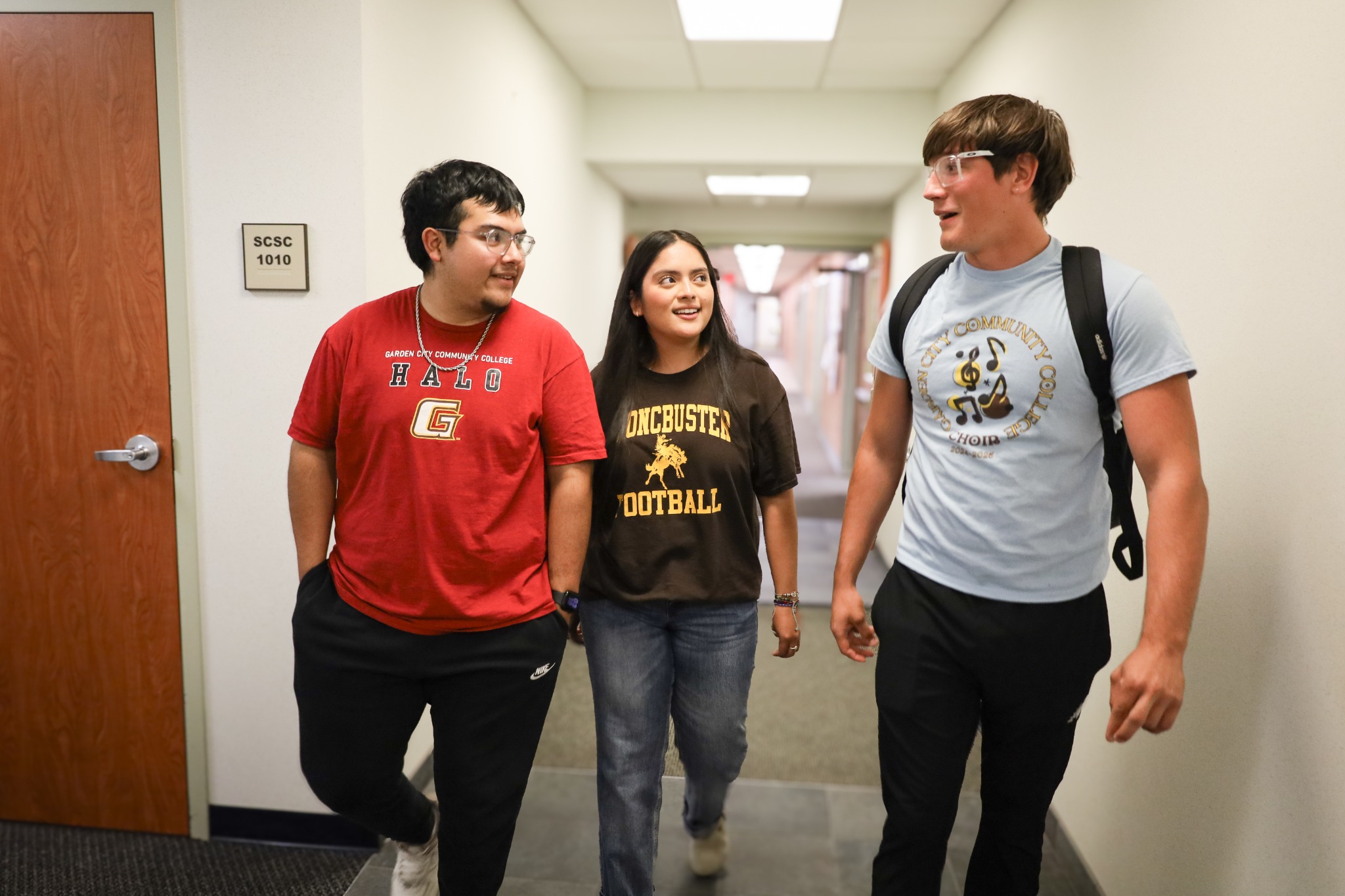 Three students walking and talking in a campus hallway between classes.